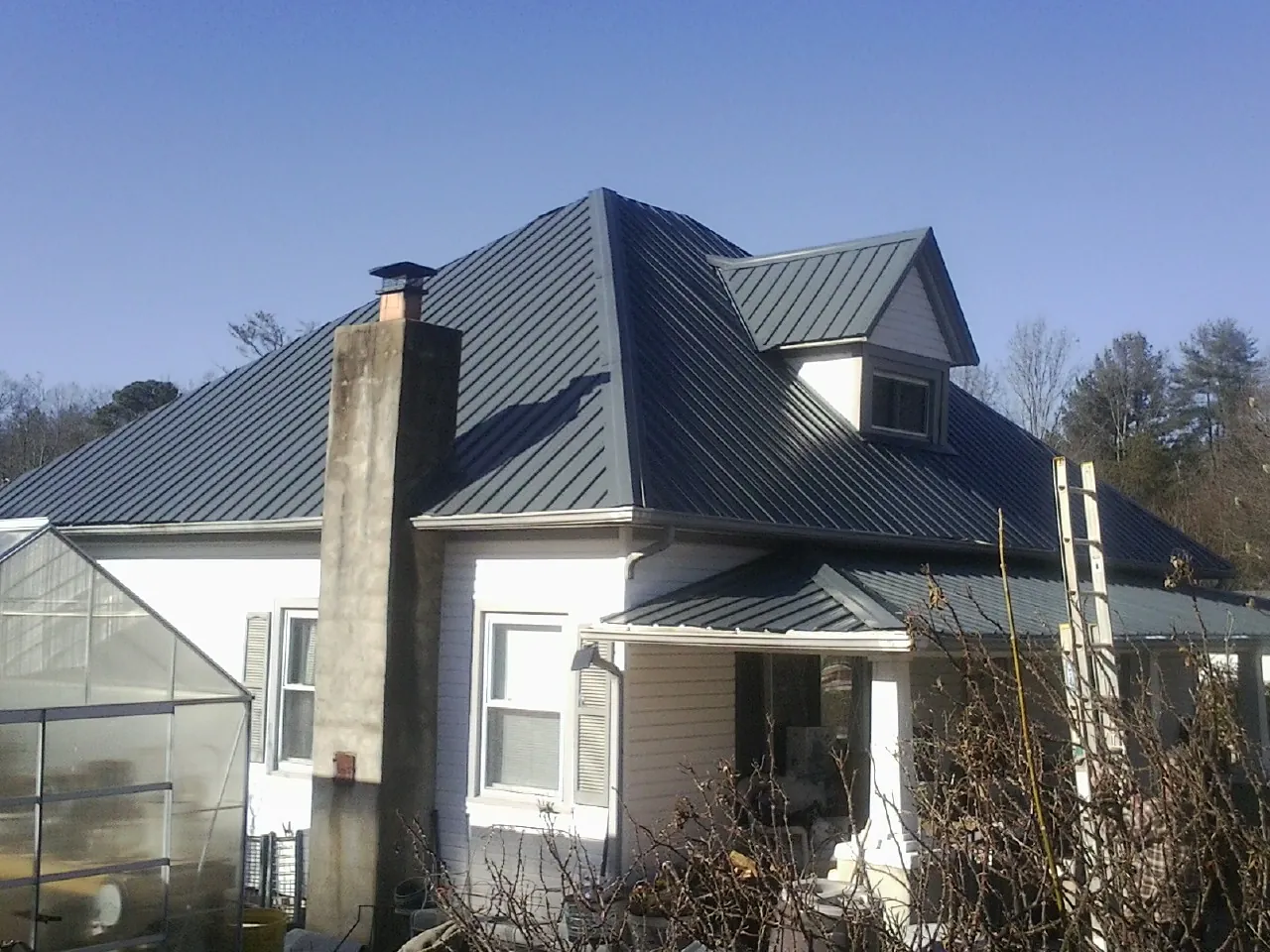 Dark blue standing seam metal roof on a white farmhouse with dormer — Slate & Tile Roof Repair by Roofing Brothers in Clarksville