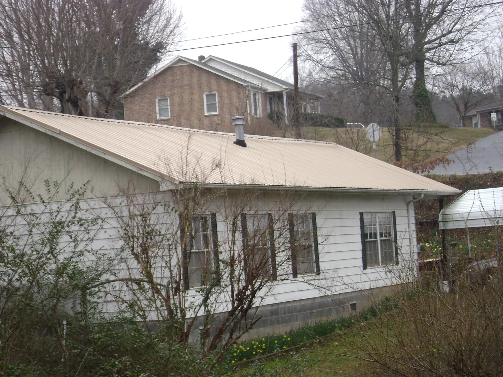 Tan metal roof on a white sided house set into a hillside — Commercial Roofing by Roofing Brothers in Clarksville